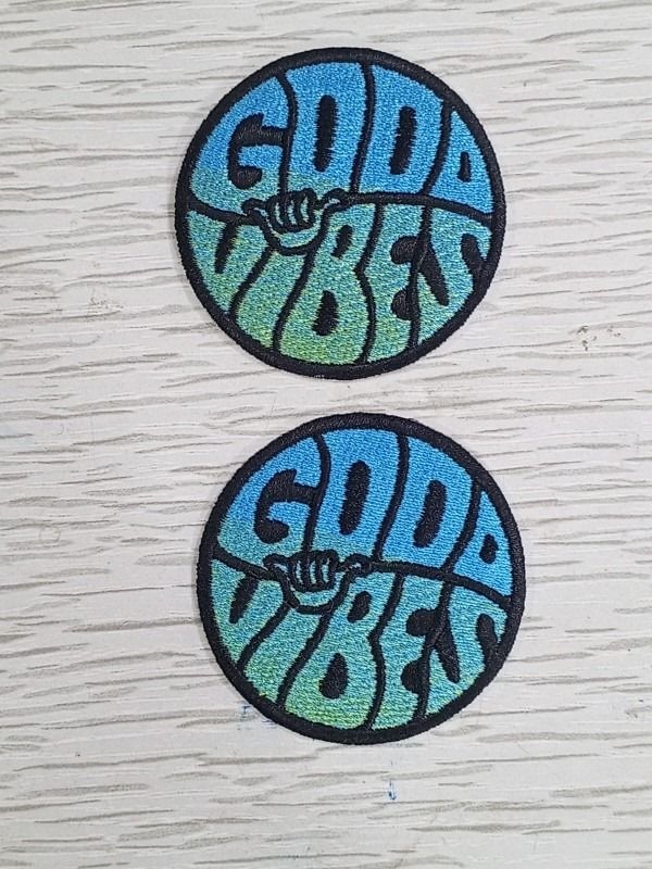 Small patch. Big personality. Two blue and green Good Vibes patches photographed on pale wood. Liberty Digitizing design with black, white and gold typography.