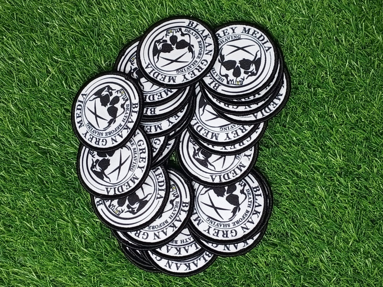 One design. Many moments. A collection of overlapping black and white circular embroidered patches on green turf. Liberty Digitizing design with black, white and gold typography.